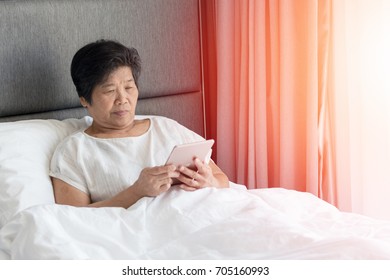 Asia old woman in bedroom using tablet on bed. Asian senior female checking social media in smartphone in healthcare center. - Powered by Shutterstock