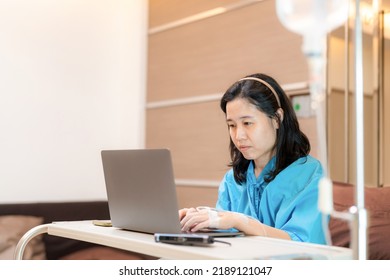 Asia Patient Woman Sitting On The Bed With Saline Solution In Hospital Ward Using Laptop, Computer And Check Email. Working In Clinic. Busy Life Of Employee During Sick. Healthcare And Medical Concept