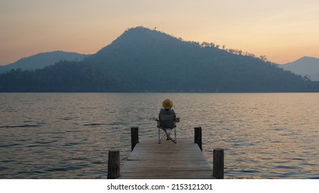 Asia people woman enjoy sit calm day dream on cozy chair at river pier hand behind head. Wide view of cloud dawn dusk sky solo budget staycation getaway at glamping take city life break stress relief. - Shutterstock ID 2153121201