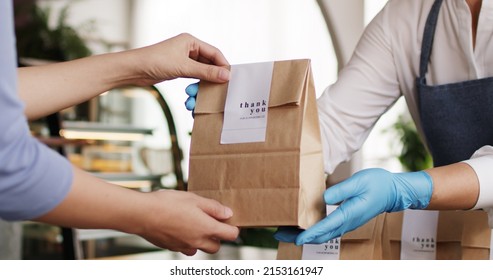 Asia people woman hand glove or face mask happy enjoy buy fast food carry send paper box pick up take home to-go lunch meal. Small cafe coffee shop work with wrap care new normal for SME omni channel. - Shutterstock ID 2153161947