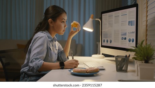 Asia people young girl work busy at home office sit on desk crave sweet junk fast food eat bite donut at night. Workforce issue bad habit stress relief by fat diet break time late dinner in hard job. - Powered by Shutterstock