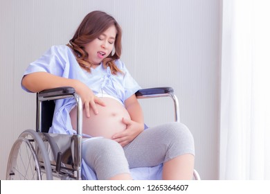 Asia pregnant woman gets false labor pain and leakage of amniotic fluid and water break maybe pregnant woman get preterm birth. It is emergency situation. Patient sits on wheelchair in hospital room - Powered by Shutterstock