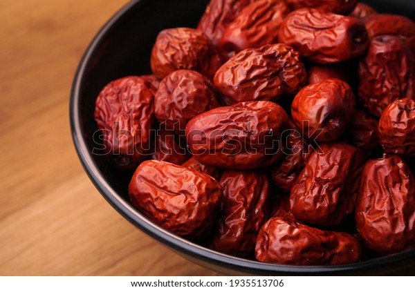 Asia red dried dates in a black bowl and wooden\
table.                          \
