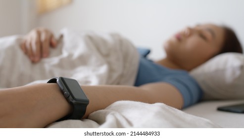 Asia Teen Woman Wear Smartwatch For Sugar Tracker, Blood Pressure Tracking, Resting Sleep Rate On Arm IoT Tech Collect Data App Device Relax Body On Cozy Bed In Future Life At Home.