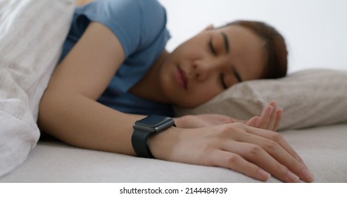 Asia Teen Woman Wear Smartwatch For Sugar Tracker, Blood Pressure Tracking, Resting Sleep Rate On Arm IoT Tech Collect Data App Device Relax Body On Cozy Bed In Future Life At Home.