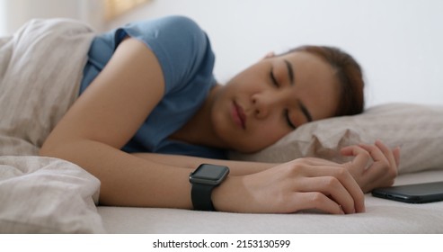 Asia Teen Woman Wear Smartwatch For Sugar Tracker, Blood Pressure Tracking, Resting Sleep Rate On Arm IoT Tech Collect Data App Device Relax Body On Cozy Bed In Future Life At Home.