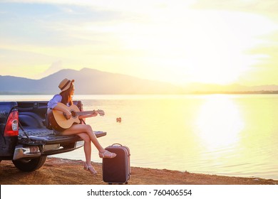 Asia traveler sitting hatchback car and playing guitar when sunset near the lake on holiday.beautiful tourist watch view of nature on vacation.