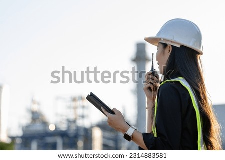 An asia woman industrial engineer in Hard Hat uses a laptop computer while standing in a heavy industrial factory in the background various metal parts project lying.