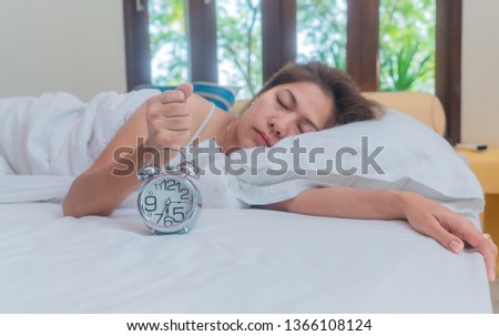 Asia woman lying in bed in the morning. She is try waking up with alarm clock. Wake up concept.