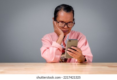 Asia Woman Old, Senior, Person Is Lonely Holding Smartphone With Online Connection To Internet Using Social Media At Home. Woman Elderly Using Smartphone To Communication With Doctor Check Health Care