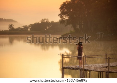 Asia woman photographer take photo on bamboo bridge in morning with orange light of sunset. 
