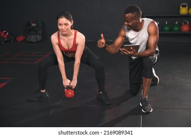 Asia woman training with kettlebell with African American trainer in fitness gym