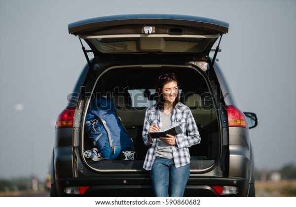 Asia woman traveler sitting on hatchback car\
with backpack
