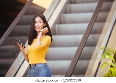 Asia woman walking and using a smart phone on escalator in a sunny summer day