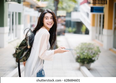 Asia woman walking and using a smart phone in the street in a sunny summer day