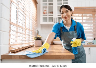 Asia woman in workwear maid cleaning home and wiping with microfiber cloth in kitchen room at home	 - Shutterstock ID 2334843207