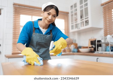 Asia woman in workwear maid cleaning home holding bottle spray and wiping with microfiber cloth in kitchen room at home	