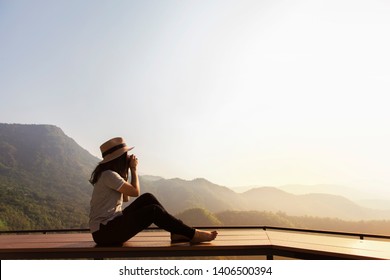 Asia Women holding a camera sitting on a wooden balcony High mountain views and nature trees.evening light