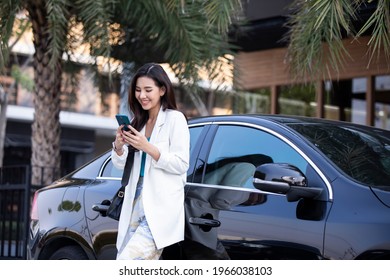 Asia Young Business Woman Driving An Electric Car And Texting Mobile Phone. A Cute Young Success Happy Brunette Woman Is Driving A Car. 