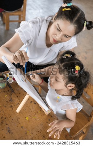 Asia young mother and little daughter drawing on canvas together. Ideas for finding activities to make children happy.

