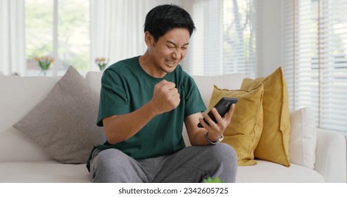 Asia young people teen man read good news message sitting at home sofa couch happy fun joy laugh smile in job hired result on mobile, award bonus, win online trade, sale order, loan money pay approve.