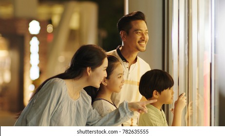 Asiam Family Laughing & Watching Store Window Outside Shopping Mall At Night