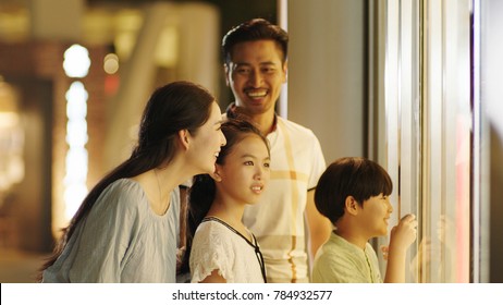 Asiam Family Laughing & Watching Store Window Outside Shopping Mall At Night