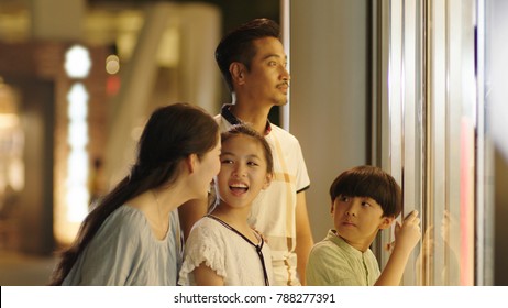 Asiam Family Laughing & Watching Store Window Outside Shopping Mall At Night