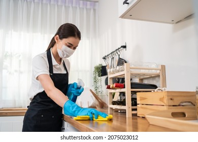 Asian Active Cleaning Service Woman Worker Cleaning In Kitchen At Home. Young Housekeeper Cleaner Wear Mask, Feel Happy And Wiping Messy Dirty Cooking Counter For Housekeeping Housework Or Chores.