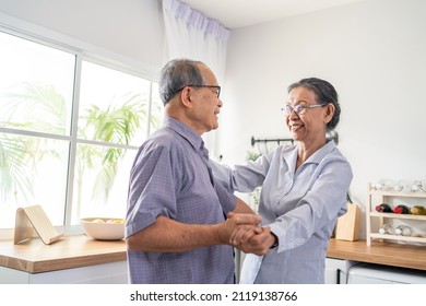 Asian Active Senior Couple Enjoy Dancing Together In Kitchen At Home. Elderly Older Grandfather And Grandmother Smiling Feeling In Love And Enjoy Relationship And Activity In House After Retirement.