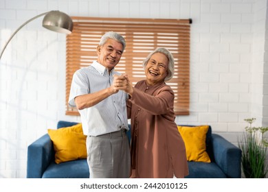 Asian active senior couple enjoy dance together in living room at home. Elderly older grandfather and grandmother smiling feeling in love and enjoy relationship and activity in house after retirement. - Powered by Shutterstock