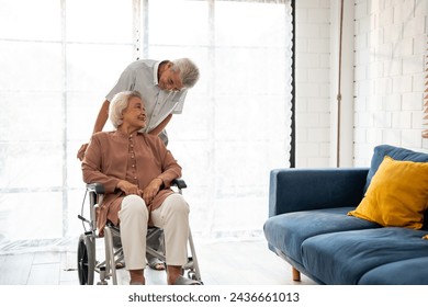 Asian active senior man support elderly woman from wheelchair to sofa. Happy family, Beautiful mature older couple doing physical therapy after retirement for health together in living room at home.
 - Powered by Shutterstock