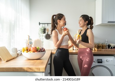 Asian active two women sibling in sportswear eat an apple in kitchen. Young beautiful girl sister feeling happy and enjoy eating fruits healthy foods to diet and lose weight for health care in house. - Shutterstock ID 2140016189