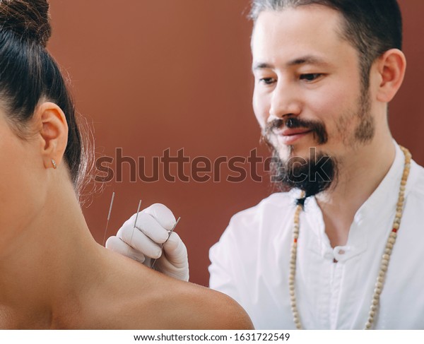 Asian acupuncturist doing acupuncture back to\
relieve woman\'s shoulder pain. Traditional Chinese medicine.\
Acupuncture needles\
close-up