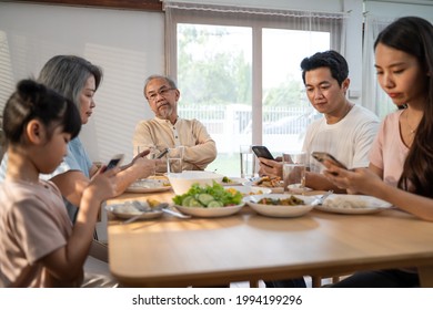 Asian Addicted Family Using Mobile Phone While Eating Breakfast Not Pay Attention To Senior Old Man. Upset Elderly Grandfather Feel Unhappy, Angry And Troubled From Ignorance Son And Daughter At Home.