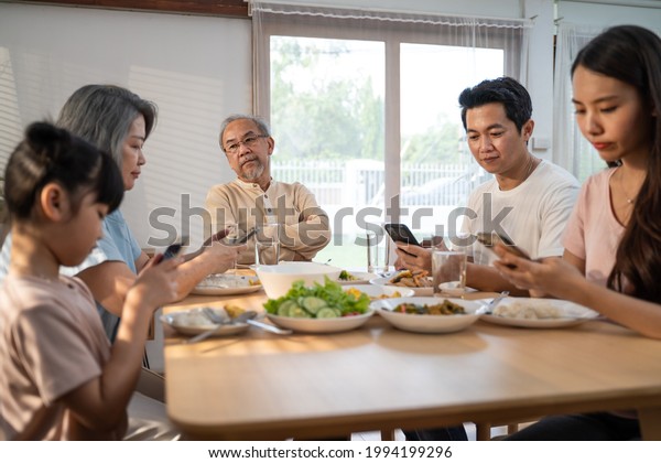 Asian Addicted family using mobile phone while\
eating breakfast not pay attention to Senior old man. Upset Elderly\
grandfather feel unhappy, angry and troubled from Ignorance son and\
daughter at home.
