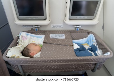 Asian adorable baby boy sleeping In special bassinet on airplane.