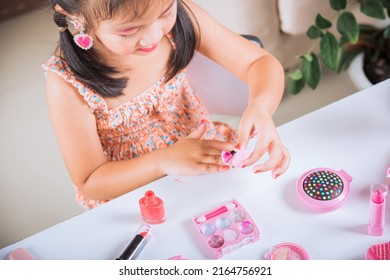 Asian adorable funny little girl making makeup dips brush into bottle to paints nails polish red nail varnish herself, Learning activity to be woman, happy kid is beautiful make up with cosmetics toy - Shutterstock ID 2164756921
