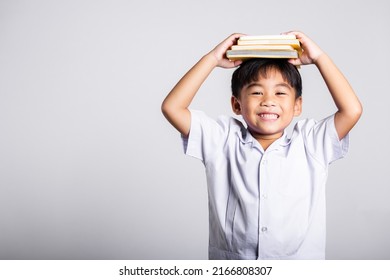 Asian Adorable Toddler Smiling Happy Wear Student Thai Uniform Red Pants Stand Holding Book Over Head And Screaming In Studio Shot Isolated On White Background, Portrait Little Children Boy Preschool