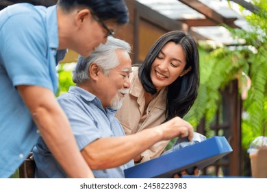 Asian adult couple surprised elderly father with gift box at outdoor cafe restaurant on summer holiday vacation. Family relationship, celebrating father's day and senior people health care concept. - Powered by Shutterstock