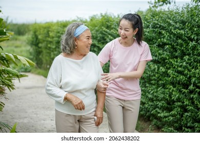 Asian Adult Daughter Hug Her Senior Mother In Backyard Garden  At Home . Young Woman Embrace Old Mom  To Take Care In Park Outdoors. 