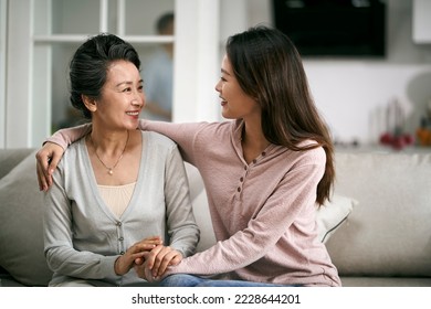 asian adult daughter and senior mother sitting on couch at home having a pleasant conversation - Powered by Shutterstock