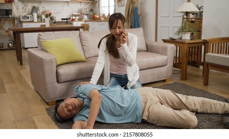 Asian Adult Granddaughter Hurrying Over To Her Fallen Grandpa In Coma On Floor And Calling 911 On Her Mobile Phone At Home. Elder Senior Fall And Faint Risk At Home Concept