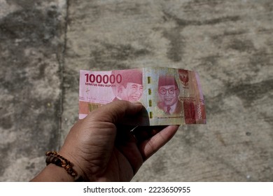 Asian Adult Male Left Hand Holding Indonesian Rupiah (100 Thousand Nominal)