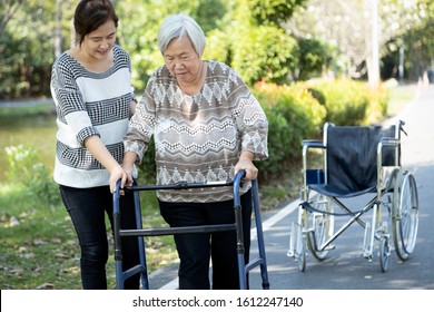 Asian Adult Woman Or Daughter Support,helping Senior Mother To Stand Up From Wheelchair,happy Elderly Patient Use Walker During Rehabilitation,practicing Walk With Female Caregiver,health Care Concept