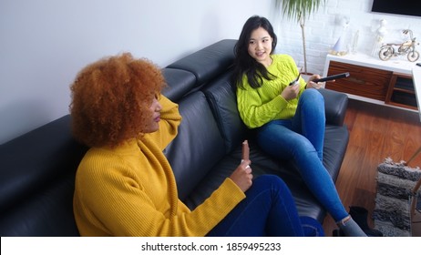 Asian And African American Woman Watching Tv And Eating Chocolate. Emotional Strees Eating Disorder, Lockdown And Mental Health Concept. High Quality Photo