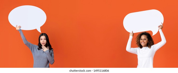 Asian and African American women wearing gray and white casual t-shirt raising speech bubbles isolated on orange background with copy space