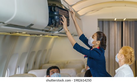 asian air hostess helping senior female caucasian passenger putting luggage into luggage cabin in airplane
