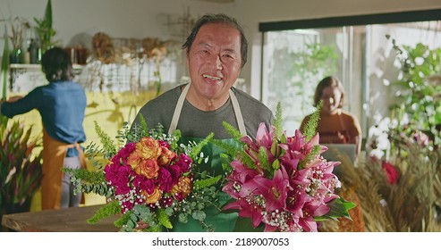 Asian American Business Entrepreneur Owner Of Flower Shop Standing Holding Two Bouquet Of Flower Arrangements Smiling At Camera