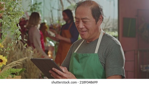 An Asian American Business Owner Using Tablet Technology Inside Small Business Store Checking Inventory Online